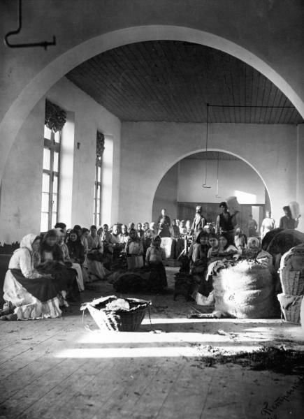 Сортировка табака, 1880-е, Екатеринославская губ., г. Ростов-на-Дону. Табачная фабрика Якова Семеновича Кушнарева. Построена по проекту и под наблюдением ростовского городского архитектора В. И. Якунина. Располагалась на углу Таганрогского проспекта и Пушкинской улицы. После прекращения производства здание использовалось как доходный дом, затем как гостиница «Палас-Отель». Сейчас – здание штаба Южного военного округа (дом 43).Выставка «Дореволюционная Россия: производство» с этой фотографией. 