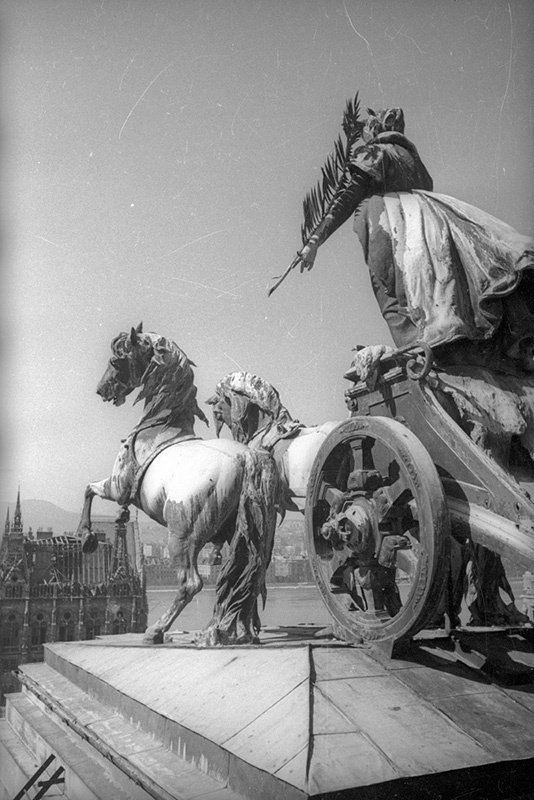 Квадрига на крыше здания бывшего Дворца правосудия, февраль 1945, Венгрия, г. Будапешт. Проект в стиле эпохи грюндерства был подготовлен архитектором Алайошем Хаусманом для конкурса проектов здания венгерского парламента, но проиграл проекту Имре Штейндля и в конечном итоге воплощен в жизнь как Дворец правосудия в 1896 году. С 1973 года в этом здании располагается Этнографический музей.