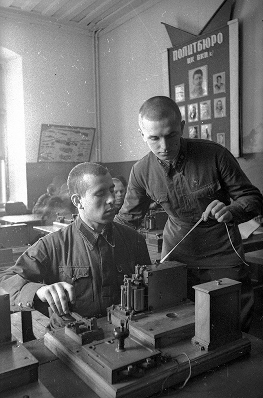 Сержант А. Пиневич, награжденный знаком «Отличник РККА», обучает молодого бойца А. Экономцева работе на аппарате Морзе, 1940 год