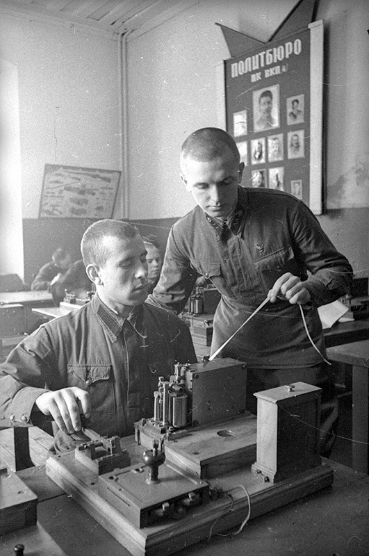 Сержант А. Пиневич, награжденный знаком «Отличник РККА», обучает молодого бойца А. Экономцева работе на аппарате Морзе, 1940 год