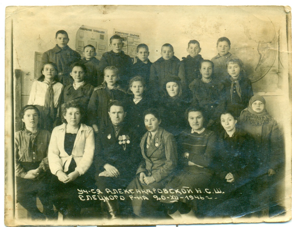 Учащиеся Александровской неполной школы, 20 декабря 1946, Елецкий р-н. Из всех школьных снимков в семейном архиве этот самый старый. Судя по подписи, он сделан 20 декабря 1946 года в Александровской неполной средней школе.К сожалению, я не знаю, кто изображен на фотографии. Кто-то из родственников по материнской линии, судя по месту. Для мамы (1964 г.р.), её сестры (1955 г.р.) и брата (1956 г.р.) слишком рано, но для ее родителей поздно.Когда училась моя мама, у школы уже был номер - № 12. Но старших классов еще не было, поэтому доучивалась мама в другом месте - школе № 5. Здание было еще то.А современную школу № 12 в Ельце с той неполной средней ничего не связывает. В том же районе, но на значительном расстоянии построено новое здание с бассейном. Учителя тоже давно все сменились. Старое здание пустовало, горело - не знаю, остался ли хоть каркас на том месте. Новая школа, естественно, полная: с первого по одиннадцатый класс.Об этой фотографии мне спросить некого. Но и молчать о ней не хочется.Фотография из архива Дарьи Ушковой.