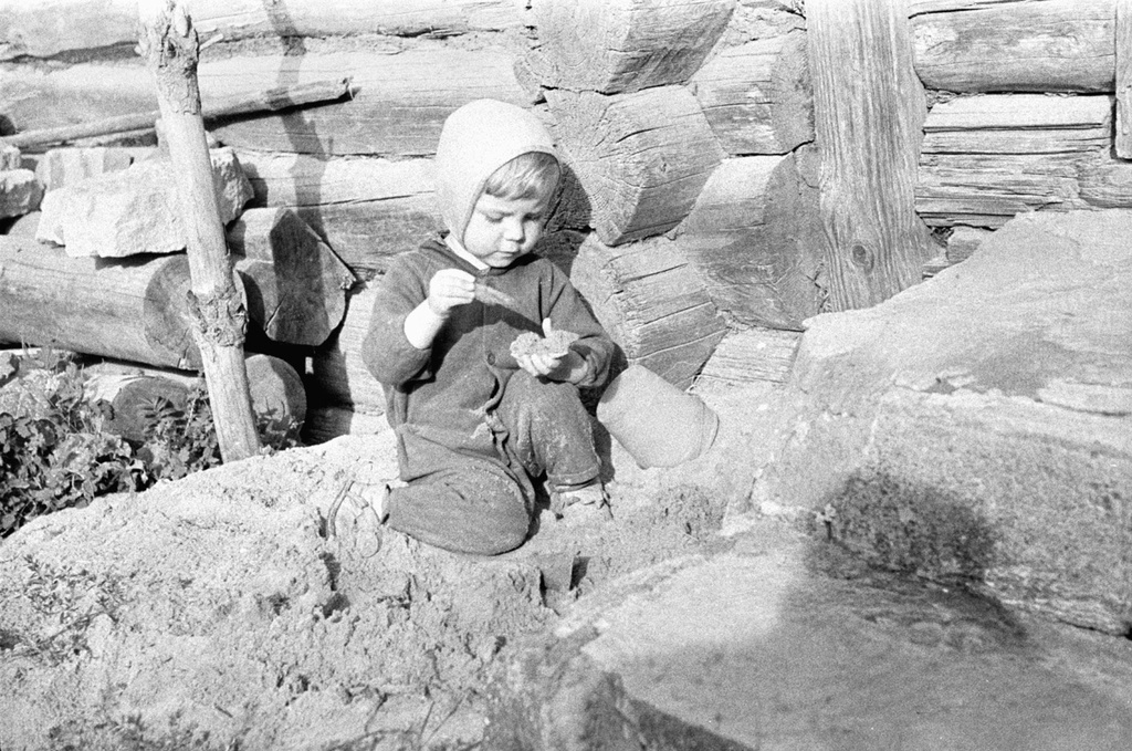 Мальчик играет на песке у стены бревенчатого дома, 1 июня 1969 - 30 августа 1969, Псковская обл., Печорский р-н, дер. Изборск. Выставка «Игра длиной в полвека» с этой фотографией.