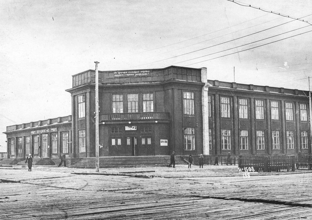 Гостиница, 10 июня 1940, Архангельская обл., г. Молотовск. Здание на перекрестке Советской и Пионерской улиц вошло в историю как ресторан «У Эдельмана». Ресторан и гостиница «Маяк» («Интурист» в годы войны) располагались в правом крыле, продуктовые и промтоварные магазины в левом крыле. Аккуратные штакетники справа –  свидетельства первых робких шагов по озеленению Молотовска. Молодые саженцы не успеют прижиться до начала войны. Массовая посадка тополей на улице Советской начнется только через десять лет.Город Молотовск в 1957 году переименован в Северодвинск. 