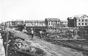 Гражданское строительство, 22 июля 1939, Архангельская обл., г. Молотовск. Слева от сланевой дороги вырыта траншея, заполненная водой. Справа от дороги – забиты сваи под строительство нескольких деревянных домов. На заднем плане – строящиеся, окруженные лесами дома и кварталы заселенных деревянных двухэтажных жилых домов. Вокруг – стройматериалы и строительный мусор.Город Молотовск в 1957 году переименован в Северодвинск. 