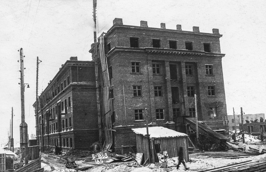 Строительство кирпичного дома, 27 февраля 1941, Архангельская обл., г. Молотовск. Вид на боковую пятиэтажную пристройку кирпичного четырехэтажного жилого дома (Первомайская, 21). Около дома возвышается деревянный подъемный кран. Справа  ведется кирпичная кладка стен трехэтажного кирпичного дома по Полярной, 1а. Около дома – стройматериалы, строительный мусор, подсобные помещения.Город Молотовск в 1957 году переименован в Северодвинск. 