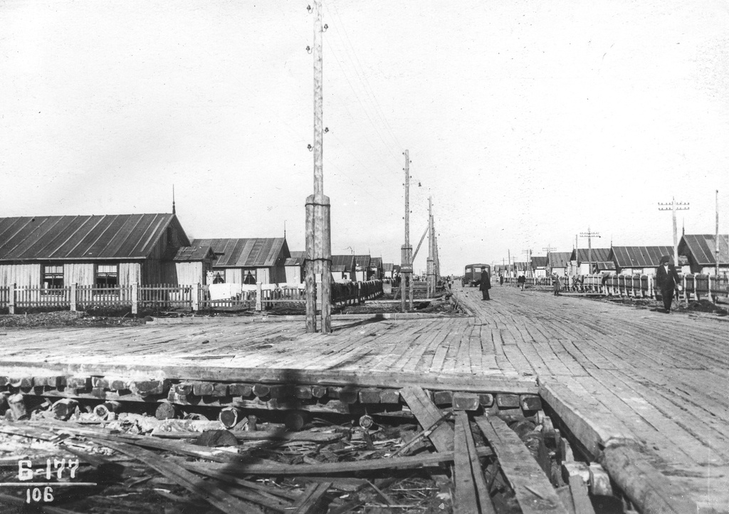 Вид улицы 6-го участка, 17 июня 1938, Архангельская обл., пос. Судострой. По обеим сторонам широкой сланевой дороги одноэтажные бараки, обращенные к дороге торцом. Территория около домов огорожена штакетником.Рабочий поселок Судострой в 1938 году получил статус города и название Молотовск. В 1957 году переименован в Северодвинск. 