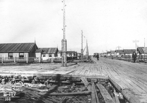 Вид улицы 6-го участка, 17 июня 1938, Архангельская обл., пос. Судострой. По обеим сторонам широкой сланевой дороги одноэтажные бараки, обращенные к дороге торцом. Территория около домов огорожена штакетником.Рабочий поселок Судострой в 1938 году получил статус города и название Молотовск. В 1957 году переименован в Северодвинск. 