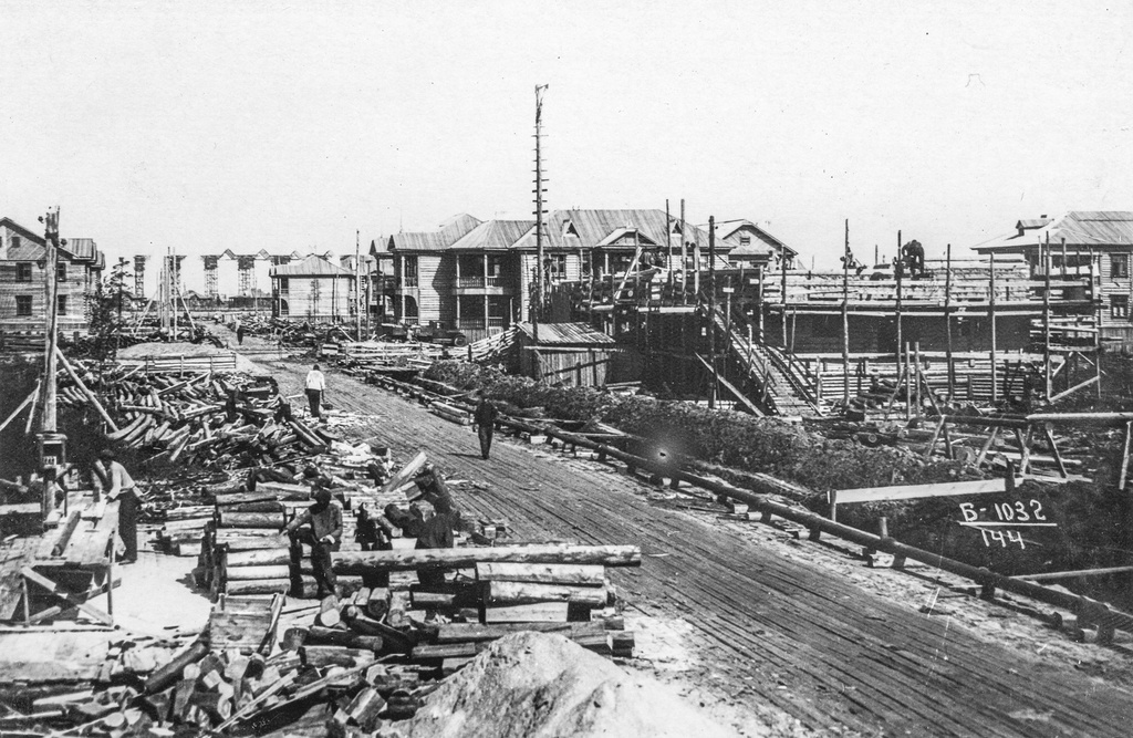 Гражданское строительство, 17 июля 1939, Архангельская обл., г. Молотовск. Фотография лета 1939 года запечатлела скоростную застройку улицы Полярной. Там, где улица берет свое начало уже видны конструкции стапельного цеха завода. Сам завод будет основан через полгода. Дома в начале улицы (до пересечения с Советской) уже построены и заселены. Возводятся срубы угловых домов по Полярной 9/37 и 10/39.  На место строительства домов по Полярной 11 и 12 уже прибыли бригады плотников. Они на месте обрабатывают пиломатериалы.Город Молотовск в 1957 году переименован в Северодвинск. 
