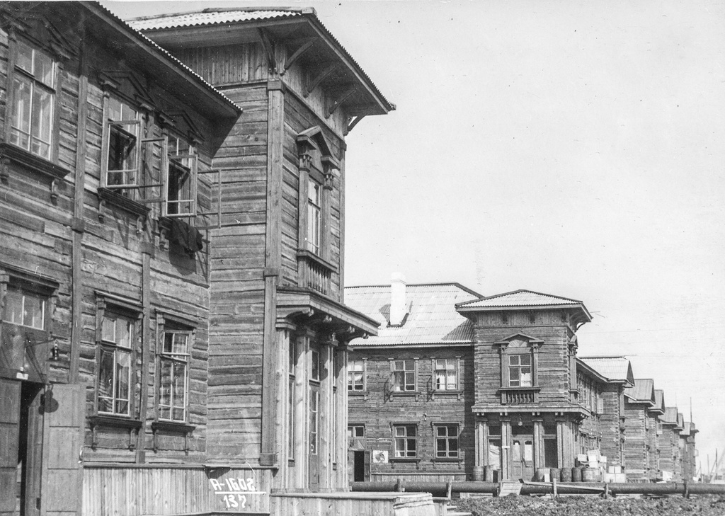 Квартал жилых домов, 13 июля 1940, Архангельская обл., г. Молотовск. На фотографии перекресток улицы Советской и Полярной. Два одинаковых дома были расположены друг напротив друга. Их украшали угловые подъезды, оформленные деревянными колоннами. Уже по планировке домов видно, что эта часть предназначалась для общественных помещений. И действительно, с конца 1930-х годов здесь действовали магазины.&nbsp;Один из домов, находящийся по адресу Советская, 40, сейчас изменился до неузнаваемости. В ходе капитального ремонта и отделки дома сайдингом угловой подъезд потерял свое архитектурное убранство. Его брат-близнец еще сохранил свои очертания. Прогуляйтесь и сравните…А если приглядеться внимательно к этой фотографии, то можно увидеть необычные трубы, которые протянулись по улице Советской. Скажем словами современника. В 1941 году специальный корреспондент газеты «Известия» Д. Попелль побывал в Молотовске и об этом написал заметку в центральной газете. «…Несколько лет назад, там, где теперь раскинулся город, были только торфяные болота, лес да песчаные отмели. Облик Молотовска своеобразен. Почти по всем его кварталам тянутся деревянные и металлические трубы. Как-будто обнажены артерии города. Поднятые более чем на метр многочисленные ответвления трубопроводов проложены ко дворам, площадям, на территории предприятий и новых строительных участков. Местами эта система приведена в действие. По трубам нагнетается вода с песком. Она бурно распространяется у выходов из труб по земле, песок осаждается на распланированной площади. Огромная территория должна быть поднята таким образом примерно на метр. На улицах и площадях песчаный покров будет укрепляться брусчаткой и гравием. Детищу сталинских пятилеток – Молотовску принадлежит важная роль в индустриальном развитии советского Севера. Население города быстро растет. Возникают новые кварталы. Преобладают двухэтажные деревянные дома с центральным отоплением, водопроводом, канализацией».Город Молотовск в 1957 году переименован в Северодвинск. 