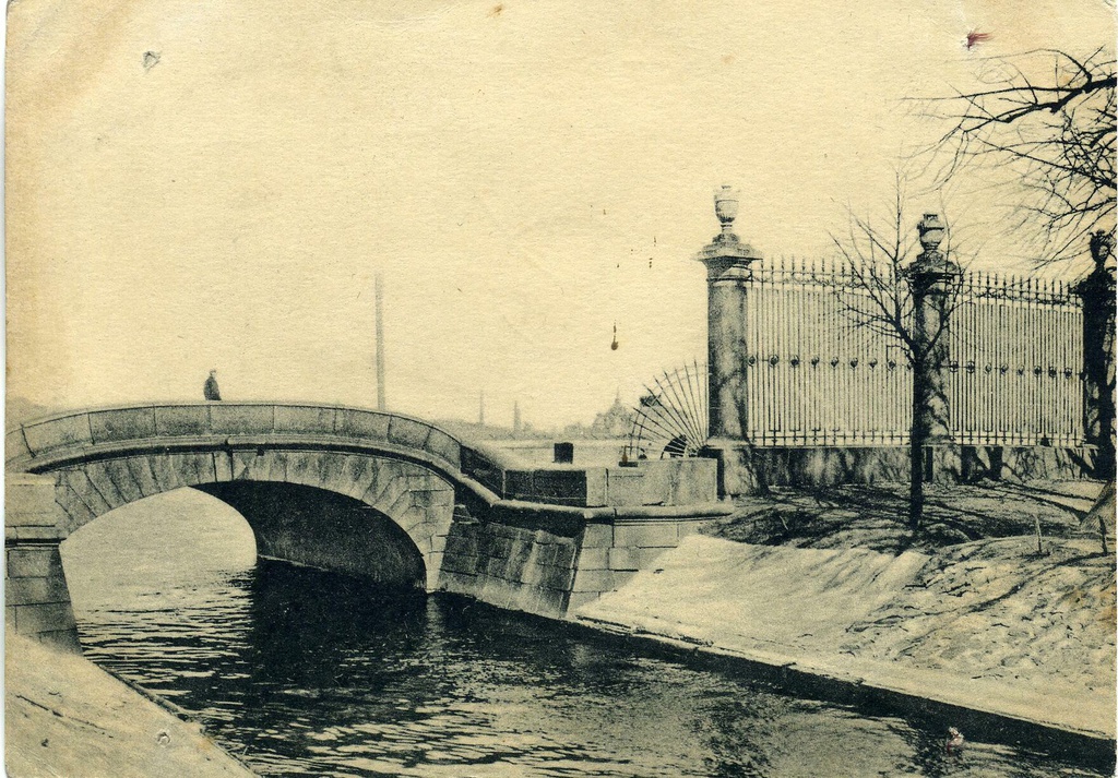 Верхне-Лебяжий мост и решетка Летнего сада, 1 января 1926 - 28 декабря 1934, г. Ленинград. Верхний Лебяжий мост расположен у истока Лебяжьей канавки и соединяет 1-й Адмиралтейский остров с островом Летний сад. Длина переправы – 12,5 метров, ширина – 30,4 метров. По конструкции это однопролетный каменный мост с параболическим очертанием свода в виде бесшарнирной арки. С фасадов мост облицован гранитом. Устои массивные каменные из бутовой кладки на свайном основании, облицованы гранитом.Лебяжью канавку прорыли в 1711–1719 годах для осушения болотистой территории, где был разбит Царицын луг (ныне Марсово поле). Канал первоначально назывался Летним, по Летнему саду, затем его переименовали в Лебяжью канавку, так как на ней стали селиться лебеди из искусственных прудов Летнего сада. В петровские времена через Лебяжью канавку было переброшено четыре деревянных моста, и первым из них стал мост, построенный в 1711–1715 годах у истока канала. Это была деревянная переправа с подъемным разводным пролетом, сооруженная по проекту голландского мастера Германа ван Болеса.В 1754 году мост перестроили в дереве. В 1767–1768 годах, в рамках строительства гранитных набережных Невы, в верховьях Лебяжьей канавки соорудили каменный однопролетный арочный мост, сохранившийся практически в неизменном виде до сегодняшнего времени. Единственное отличие: изначально на устоях моста были устоновлены газовые фонари. Предположительно к концу XIX века фонари были утрачены.Проект переправы разработали архитектор И. Л. Росси и «квадраторного дела мастер» Т. И. Насонов. Мост назвали Лебяжьим (так же назывался в то время и Нижний Лебяжий мост).