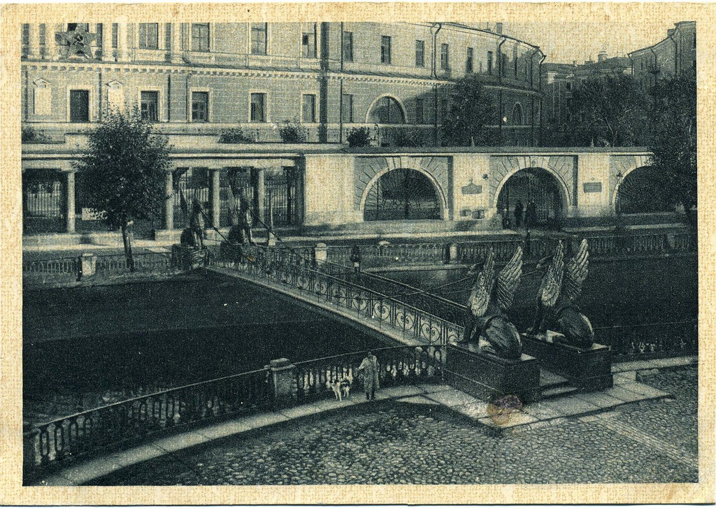 Ленинград. Львиный мостик на канале Грибоедова (№ 57), 1929 год, г. Ленинград. Название – «Львиный», на самом деле «Банковский мост», принадлежит пешеходному мосту, перекинутому через канал Грибоедова около здания Санкт-Петербургского государственного экономического университета, который соединяет Казанский и Спасский острова.Мост однопролетный балочный длиной 28 метров, шириной – 3,1 метра.Банковский мост – выдающийся памятник мостостроительной архитектуры первой четверти XIX века. Один из трех сохранившихся пешеходных цепных мостов в Петербурге (наряду с Львиным и Почтамтским мостами). Названный по расположенному рядом Ассигнационному банку, мост был открыт для пешеходного движения 24 июля (5 августа н.с.) 1826 года, и по нему в тот день прошли свыше 9 тысяч человек.  Мост предназначен для пропуска пешеходов и является одним из шести висячих мостов, построенных в 1823–1826 годах.Первый висячий мост (ныне не существует) был построен по проекту инженера П. П. Базена в 1823 году в парке «Екатерингоф», а остальные 5 мостов (два транспортных: Египетский и Пантелеймоновский – ныне оба перестроены, 2 пешеходных: Почтамтский и Львиный – ныне оба перестроены, и Банковский, тоже пешеходный) были построены по проектам инженера Г. М. Треттера. Почтовая открытка № 57 издательства ГИЗ, Главлит № А – 38751 по фотографии Владимира Владимировича Преснякова