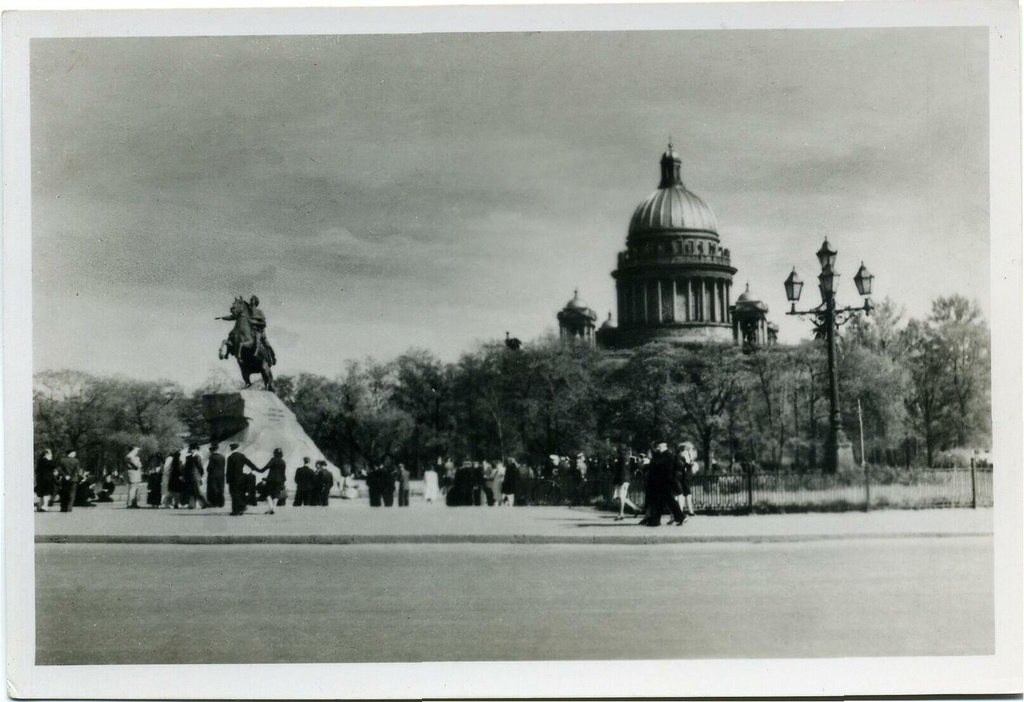 Площадь Декабристов, 1956 год, г. Ленинград. Площадь Декабристов, в настоящее время  Сенатская площадь в Санкт-Петербурге. Одна из центральных площадей города и архитектурный ансамбль, сформированный Адмиралтейством, зданием Сената и Синода и Александровским садом. Площадь начала формироваться сразу после строительства Адмиралтейства в 1704 году, первоначально являясь гласисом крепостных сооружений вокруг верфи. Однако, свое историческое название она получила только в 1763 году после переезда в дом А. П. Бестужева-Рюмина, расположенный возле площади, Правительствующего Сената. Вид на Исаакиевский собор, памятник Петру I (Медный всадник).                                                                           Открытое письмо издательства&nbsp;«Ленфотохудожник», 1956 год, № М-22104.