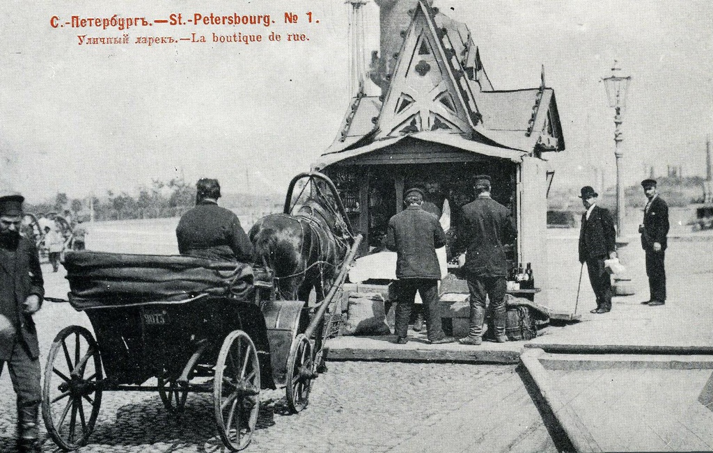 Уличный ларек (№ 1), май - июнь 1903, г. Санкт-Петербург. В мае–июне 1903 года, в дни празднования 200-летия Петербурга, журнал «Родина» заказал фотографу Н. Н. Ольшевскому снимки для юбилейного очерка. Эти фотографии издательство и выпустило в виде серии из 100 нумерованных открыток. Все снимки сделаны в небольшой промежуток времени и дают «срез» жизни города. Ольшевский решает свою задачу неординарно: смело вводит в кадр живые бытовые детали, уличные сцены, типы городских жителей. Снимая архитектуру, он ищет неожиданный ракурс, фотографирует  недостроенные здания – ведь «строительный бум» один из характернейших признаков петербургской жизни того времени.Открытки для издания любезно предоставил ленинградский коллекционер Н. П. Шмитт-Фогелевич.Ларек расположен прямо у Ростральной колонны. Это напоминает о старой петербургской традиции, когда с началом навигации Биржевая площадь превращалась в своеобразный рынок: здесь шла когда-то бойкая торговля с только что прибывших отечественных и иностранных кораблей.Выпуск № 1 «Образы старого Петербурга» издательства «Ленинградское отделение Советского фонда культуры», 1989 год, заказ № 3176 от 05.05.1990 года. Составители серии: А. В. Кобак, Т. Б. Притыкина, Н. П. Шмитт-Фогелевич