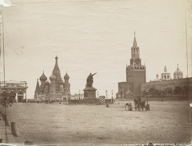 Красная площадь, 1880 - 1890, г. Москва. На снимке изображена Красная площадь. Слева видны Верхние торговые ряды, построенные архитектором О. Бове в 1815 году. Правее торговых рядов виден собор Покрова Пресвятой богородицы, что на Рву (собор Василия Блаженного). Правее собора видно здание Кремлевского подворья. В правой части снимка видна Спасская башня Кремля и стоящие по сторонам Спасских ворот часовни: слева&nbsp;– Великого Совета Откровение (Смоленская), справа&nbsp;– Великого Совета Ангел (Спасская). За кремлевской стеной видны купола церкви Святого Михаила Малеина и церкви Святой Екатерины в Вознесенском монастыре. В центре Красной площади стоит памятник Минину и Пожарскому, окруженный четырьмя фонарями. Справа от памятника стоит полосатая будка, в которой находился охранявший памятник гренадер. Памятник окружен ажурной чугунной решеткой. По площади едут телеги и коляски, идут прохожие.