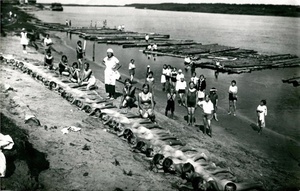 Пионеры принимают солнечные ванны на берегу реки Шексна, 6 июля 1935, г. Череповец. На фотографии обнаженные мальчики и девочки из городского пионерского лагеря на базе школы № 2 города Череповца принимают солнечные и воздушные ванны перед купанием в реке. В данном случае педагоги решили не делить учеников 5-6 классов по половому признаку (возможно, по причине отсутствия среди педагогов мужчин), поэтому мероприятие проводится совместно. В 1934 году школа № 2 имела 4 отделения (933 ученика). Директором школы был Георгий Федорович Кармановский. В школе проводилась большая общественная работа, развернулось пионерское движение. 85% учащихся входили в состав пионерской и комсомольской организаций.