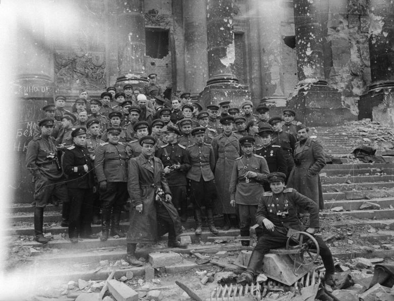Группа советских военных и корреспондентов на фоне Рейхстага, май 1945, Германия, г. Берлин. В центре в кожаном плаще – военный фотокорреспондент Георгий Петрусов.