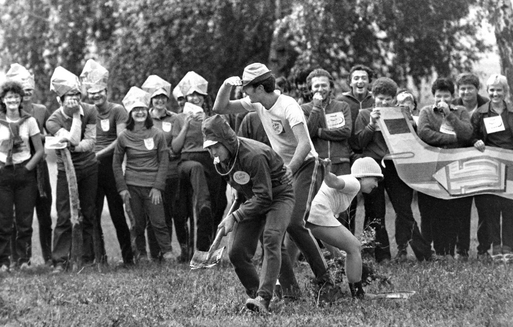 «Нарушители государственной границы СССР», июль 1984, Новосибирская обл., станция Восточная. Турслет. Показательные выступления.Группа шпионов пытается проникнуть на территорию СССР. Ведущий с лопатой ищет лазейку, девушка в ластах ветками заметает следы. Зрители с макетом самолета – команда городского аэропорта Новосибирск-Северный. В 2011 году аэропорт был закрыт.Выставка «В Новосибирске Сергея Секретарева» с этой фотографией.