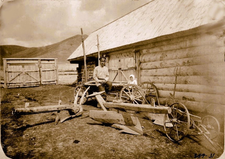 Хозяйственный двор у сибирских казаков, 1909 год, Семипалатинская обл.. На снимке из альбома «Сибирские казаки на службе и в быту» 1911 года изображен хозяйственный двор у сибирских казаков, с деревянными постройками – амбаром и высокими воротами, а также телегой и плугом типа казачьей колесной сохи, характерной для степных районов южной Сибири и киргизской степи. Сибирские казаки, пришедшие в конце 1840-х годов на реку Копалку, использовали именно такую же сельхозтехнику и возводили аналогичные хозяйственные постройки, в том числе, на первых порах, и деревянные заборы.