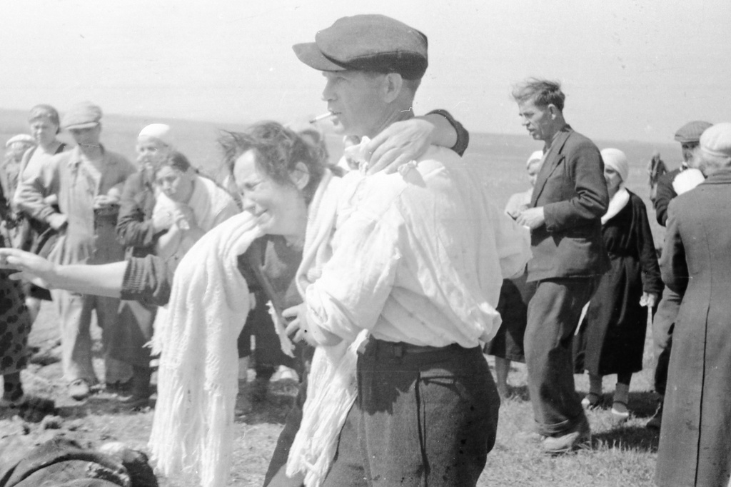 Эксгумация тел узников концлагеря «Красный», 21 - 23 апреля 1944, Крымская АССР, Симферопольский р-н, совхоз «Красный». Концлагерь «Красный» находился на территории птицесовхоза «Красный» под Симферополем  (место заключения советских военнопленных и гражданских лиц в период с ноября 1941 по апрель 1944 года). Из монтажного листа кинооператора: «Доронкина Евгения Лаврентьевна (в бел. платке) опознала мужа Доронкина Ивана Федоров., 45 лет, техник стройконторы г. Симферополь».Выставка «Партизаны Крыма» с этой фотографией.