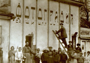 Фотография Б.А. Шишлянникова, 1922 - 1923, г. Владикавказ. «Фотография Б.А. Шишлянникова» на старом городском рынке.  На фото: времена НЭПа, создание рекламной надписи&nbsp;«Фотография Б.А. Шишлянникова» для фотоателье Бориса Александровича.Для рекламы используется помещение в высоким фасадом, над словом «Фотография» видны дырки от старой вывески или рекламы. Справа – сам вход в&nbsp;«Фотографию» (фотоателье), слева от входа – выставочный стенд с образцами фоторабот.Примерно с середины 1920-х годов, Борис Александрович Шишлянников стал подписывать свои фотоработы псевдонимом «БАШ» (И.О.Ф.): «Борис Баш». Потом псевдоним стал фамилией.