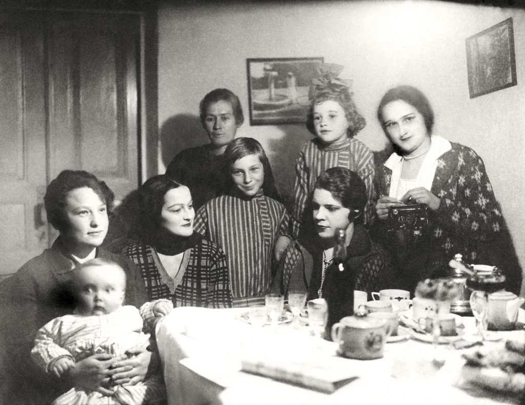 Жена, ее сестра, хозяйка дома, приятельницы и дети хозяйки, 1929 год, Туркменская ССР, г. Ашхабад. На фото: жена (вторая слева), ее сестра (крайняя справа), хозяйка дома (в центре, слева от картины), приятельницы и дети хозяйки. Перед сестрой на штативе стоит фотоаппарат.