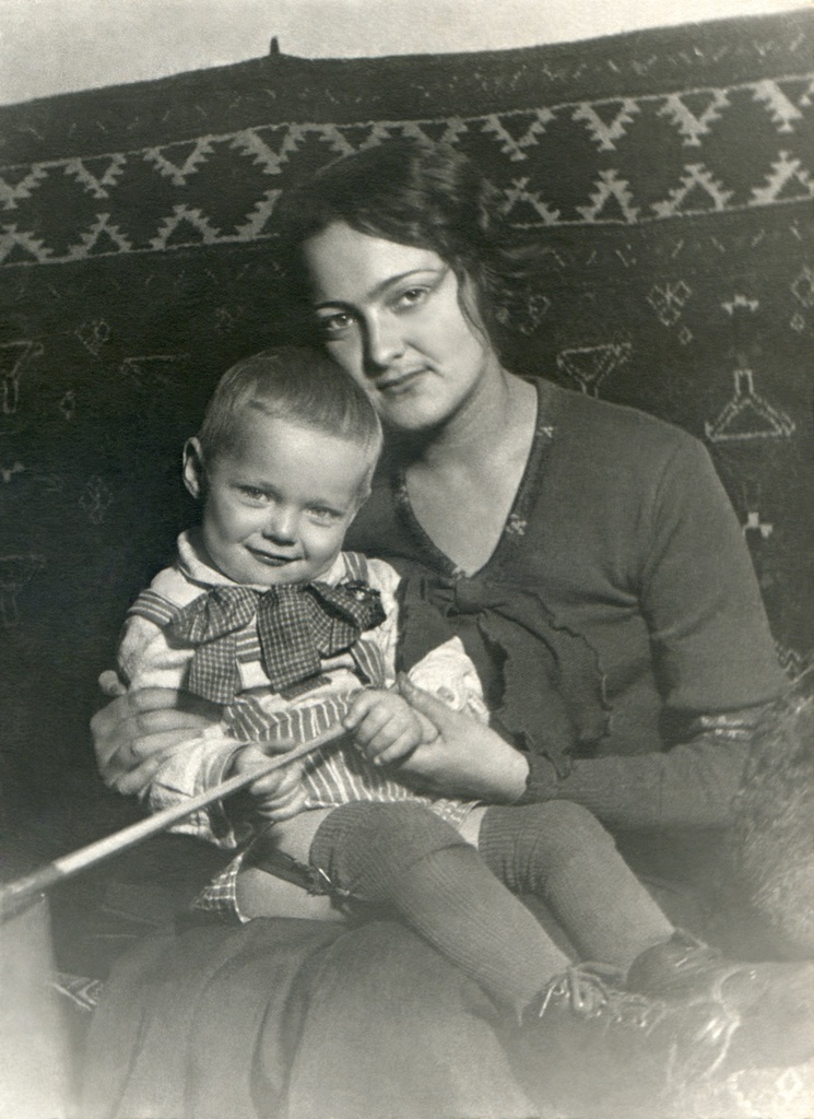 Портрет жены и сына в комнате, 1935 год, г. Москва. Комната на верхнем этаже в коммунальной квартире, метров 15-20, где жил автор с женой, сыном и тещей. На стене висит туркменский ковер ручной работы. Автор – Борис Александрович Баш (Шишлянников) (1901–1942), фотограф, кинооператор и режиссер.