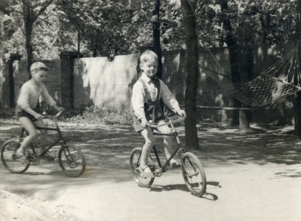 Гонки вокруг клумбы. Портрет сына (справа) во дворе дома 10 на Житной улице, 1938 год, г. Москва. Огороженный двор старого дома 10 на Житной улице, где жила семья автора. Виден забор, уходящий влево и часть клумбы, вокруг которой катаются сын автора (6 лет) и соседский мальчишка позади. Автор – Борис Александрович Баш (Шишлянников) (1901–1942), фотограф, кинооператор и режиссер.