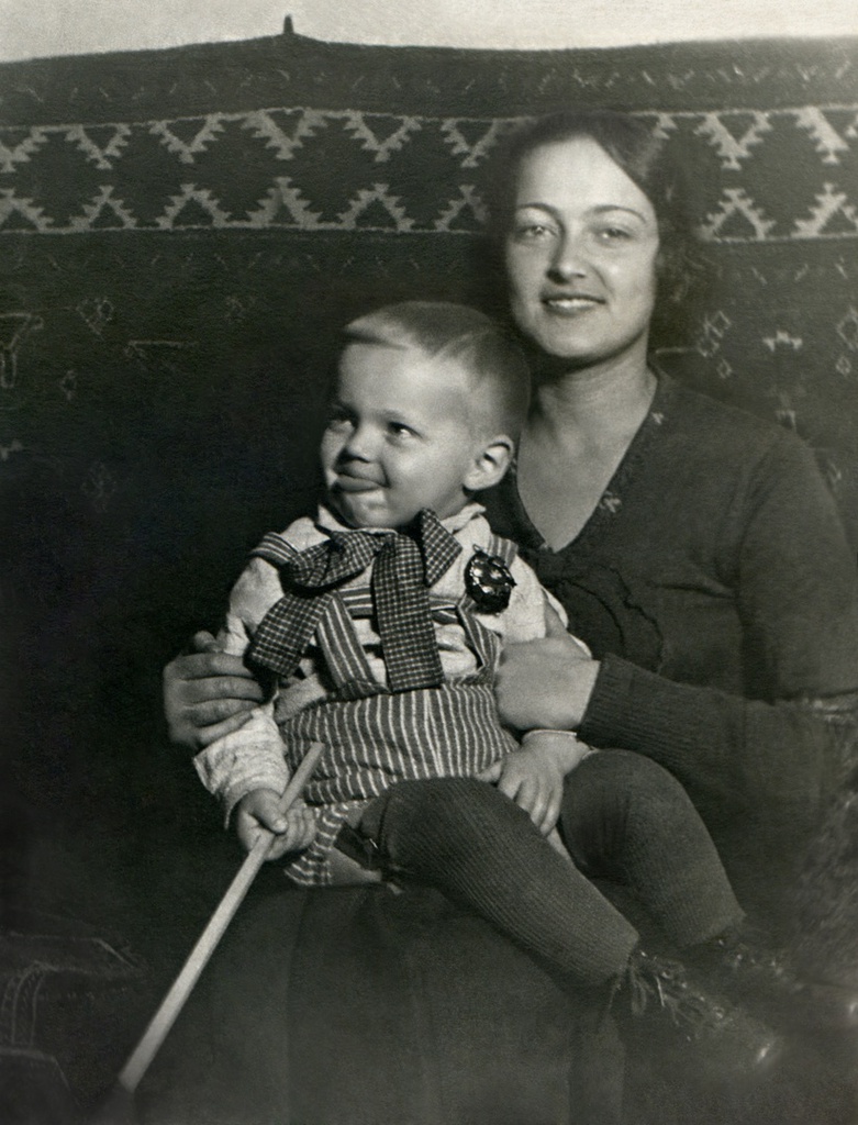 Портрет жены и сына в комнате, 1935 год, г. Москва. Комната на верхнем этаже в коммунальной квартире, метров 15-20, где жил автор с женой, сыном и тёщей. На стене висит туркменский ковер ручной работы. Автор – Борис Александрович Баш (Шишлянников) (1901–1942), фотограф, кинооператор и режиссер.