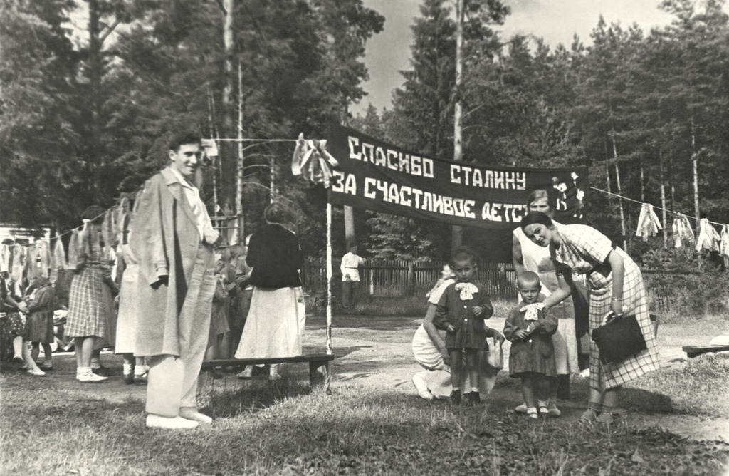 Портрет жены и сына (крайние справа) в летнем детском саду, 1936 год, Московская обл., Раменский городской округ, Верейское сельское поселение. На обороте фото подпись: «Удельная, детсад». Позади жены стоит домработница Лида. Точка съёмки выбрана условно. Автор – Борис Александрович Баш (Шишлянников) (1901–1942), фотограф, кинооператор и режиссер.