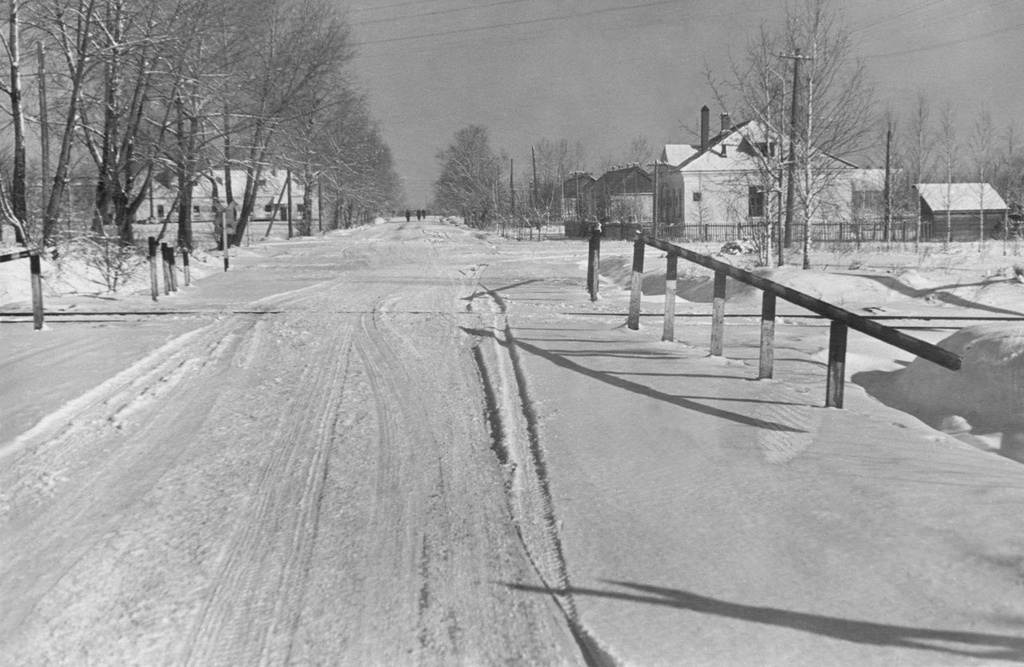 Зимой на ж/д переезде, 1 декабря 1957 - 28 февраля 1958, Белорусская ССР, Могилевская обл., Быховский р-н, г. Быхов. 57-я МРАД (морская ракетоносная авиационная дивизия). Гарнизон города Быхова: здание за переездом справа – коммутатор батальона связи, дальше, по этой же стороне стоят два барака ОМИС (Отделение морской инженерной службы), на левой стороне была пожарная часть.