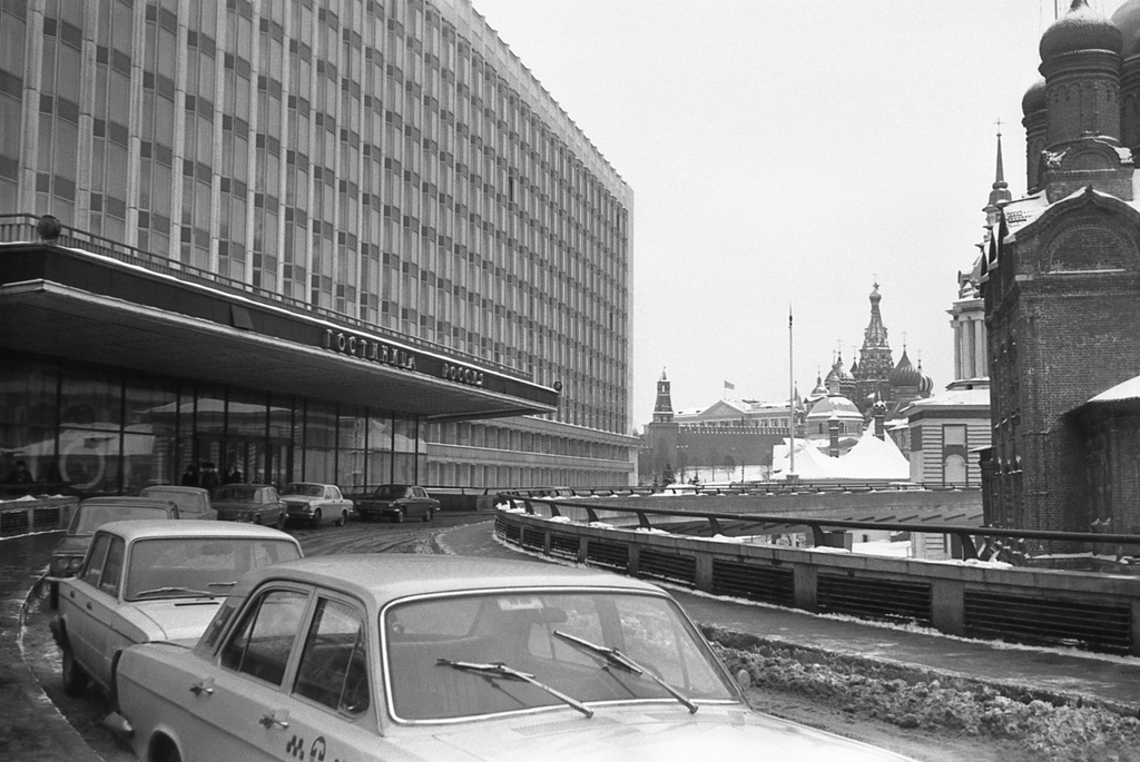 Гостиница «Россия», 1974 - 1975, г. Москва. Слева – один из подъездов гостиницы «Россия» со стороны ул. Разина (сейчас – ул. Варварка). Справа, по мере удаления: Знаменский собор, колокольня Знаменского собора, Старый Английский двор, церковь святой Варвары, Покровский собор (за ним спряталась Спасская башня, видна звезда) и 14-й корпус Московского Кремля с флагом (снесен в 2016 году) за Кремлевской стеной. Позади, за кадром – церковь Георгия Победоносца на Псковской горке.