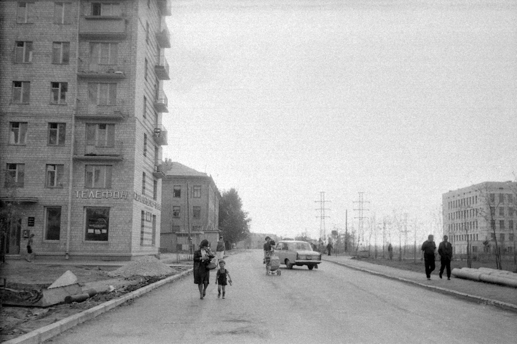 Свиблово. Улица Седова, дом 7 корпус 1. Почтовое отделение «И-323», 1966 год, г. Москва. Слева: дом 7 корпус 1 по улице Седова. На первом этаже – почта «И-323» (справа после входа внутрь), в левой половине был переговорный пункт с телефонными кабинами (межгород). Благоустройство еще не закончено, дом сдан только в 1965 году. Далее, слева – овощная палатка перед трехэтажным домом 9 корпус 1. Слева за кадром: дом 5 корпус 1 (12-эт. башня с овощным магазином), во дворе – знаменитый дом 5 корпус 2 (в нем снимали кинофильм «Операция Ы и другие приключения Шурика», часть «Напарник»), в который автор переедет с женой и сыном в 1970 году. Вдали, прямо, дом 13 по Лазоревому проезду и старая усадьба на Свибловских прудах. Справа: на тротуаре остановка 117 автобуса (в сторону конечной на ВДНХ) и школа № 294. Слева по дороге идет жена автора с сыном Вадимом (4 года).