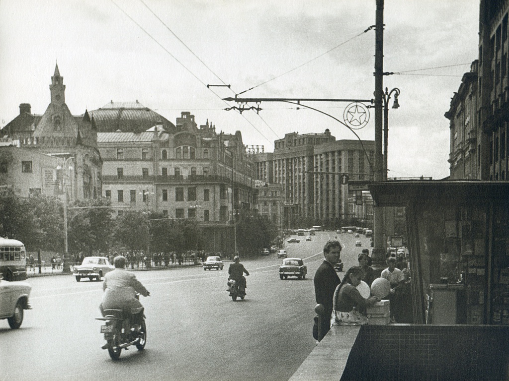 Театральный проезд, 1960 год, г. Москва. Проспект Маркса в 1961–1990 годах, сейчас – Театральный проезд. Слева: Третьяковские ворота (с башней) и начало одноименного проезда, потом гостиница «Метрополь». По центру: здание Госплана (сейчас – Государственная Дума РФ). Справа: журнальный киоск между двумя спусками в подземный переход на другую сторону дороги, чуть дальше – остановка троллейбуса. За кадром справа – магазин «Детский мир».