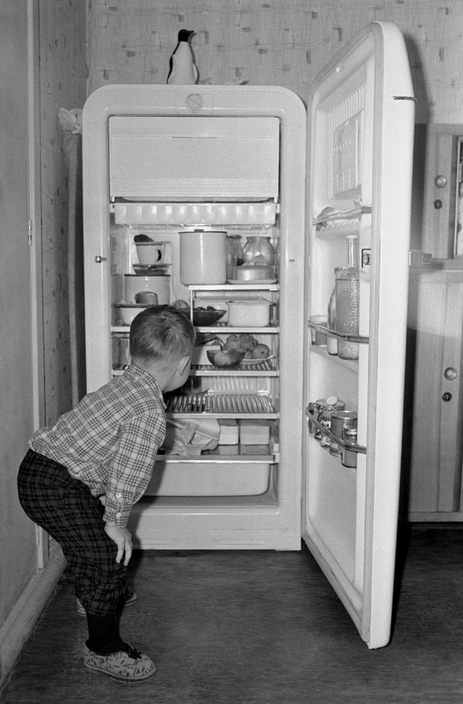 Портрет сына у семейного холодильника ЗиЛ «Москва», 1965 год, г. Москва. Маленькая комната в 3-комнатной квартире, которую использовали как столовую; слева от холодильника – гладильная доска,  на верху стоит кувшин «Пингвин», справа – буфет.