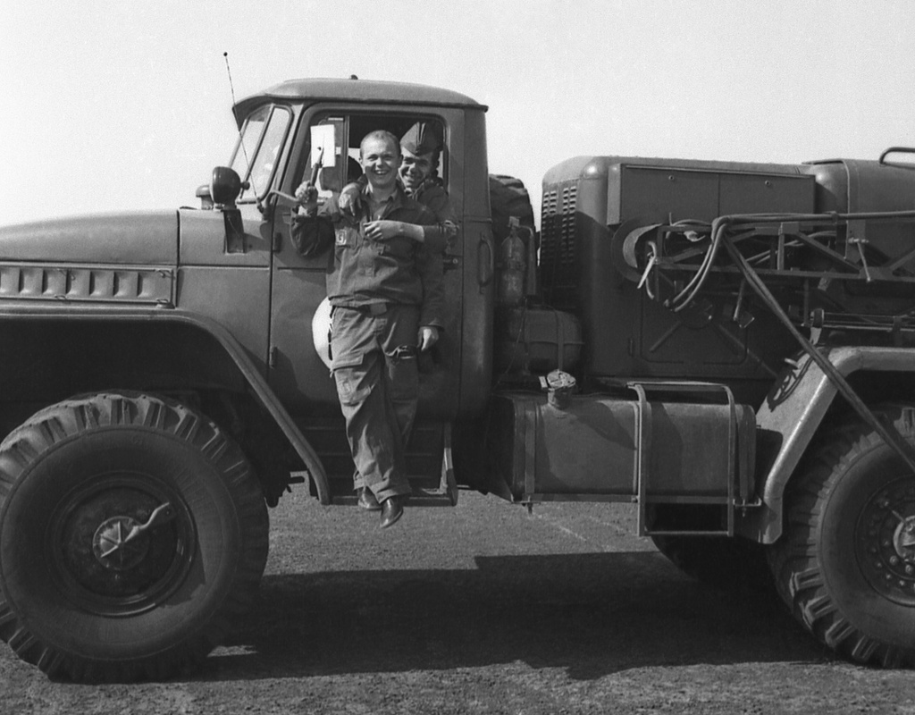 Полеты на грунтовом аэродроме в Кирсанове, 643 уап ТВВАУЛ, июнь - август 1982, Тамбовская обл., Кирсановский муниципальный округ, Голынщинский сельсовет. АОшник 1-й эскадрильи Вадим Баш (слева) на подножке АПАшки.643 учебный авиаполк ТВВАУЛ (в/ч 42149, база: город Тула, аэродром Клоково, самолеты Л-29). На лето авиаполк перелетал из Тулы в Кирсанов и Новгородовку Тамбовской области (по две эскадрильи на каждый город).ТВВАУЛ – Тамбовское высшее военное авиационное училище летчиков имени М. М. Расковой.Часть расформирована в 1990 году, потом в 1995 году закрыли и Тамбовское ВВАУЛ.АПАшка (жен. род, сленг летчиков и техсостава): АПА-5Д, Аэродромный Передвижной электроАгрегат, на базе Урал-4320 (на фото), является автономным источником электрической энергии и предназначен для одиночного и группового электростартерного запуска авиационных двигателей, питания бортовой электроаппаратуры самолетов в наземных условиях, а также для буксировки самолетов.АОшник (сленг) – техник группы АО (авиационного оборудования), специалист, отвечающий за исправность электрических и приборных систем воздушного судна.