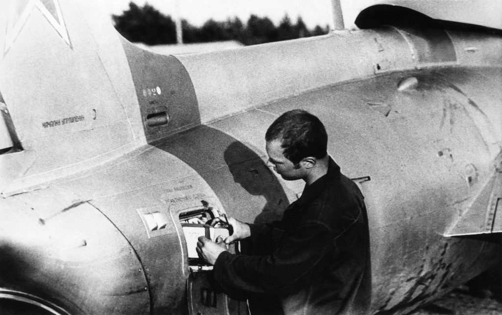 Полеты на грунтовом аэродроме в Кирсанове, 643 уап ТВВАУЛ, июнь - август 1982, Тамбовская обл., Кирсановский муниципальный округ, Голынщинский сельсовет. АОшник 1-й эскадрильи Вадим Баш (срочник) меняет кассету с пленкой в САРПП-12. В правой руке – отвертка, указательный палец на защелке кассеты.643 учебный авиаполк ТВВАУЛ (в/ч 42149, база: город Тула, аэродром Клоково, самолеты Л-29). На лето авиаполк перелетал из Тулы в Кирсанов и Новгородовку Тамбовской области (по две эскадрильи на каждый город).ТВВАУЛ – Тамбовское высшее военное авиационное училище летчиков имени М. М. Расковой.Часть расформирована в 1990 году, потом в 1995 году закрыли и Тамбовское ВВАУЛ.САРПП-12 – система автоматической регистрации параметров полета. Запись параметров ведется на фотопленку в металлической кассете. После полета кассету с записью снимали и заменяли на новую, с чистой пленкой.АОшник (сленг) – техник группы АО (авиационного оборудования), специалист, отвечающий за исправность электрических и приборных систем воздушного судна.