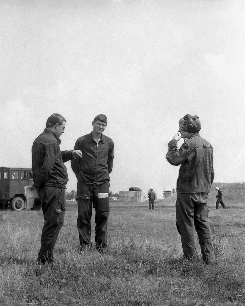 Полеты на грунтовом аэродроме в Кирсанове, 643 уап ТВВАУЛ, июнь - август 1982, Тамбовская обл., Кирсановский муниципальный округ, Голынщинский сельсовет. Летчики-инструкторы на аэродроме перед началом полетов. Справа, в шлемофоне – старший лейтенант Алешин.643 учебный авиаполк ТВВАУЛ (в/ч 42149, база: город Тула, аэродром Клоково, самолеты Л-29). На лето авиаполк перелетал из Тулы в Кирсанов и Новгородовку Тамбовской области (по две эскадрильи на каждый город).ТВВАУЛ – Тамбовское высшее военное авиационное училище летчиков имени М. М. Расковой.Часть расформирована в 1990 году, потом в 1995 году закрыли и Тамбовское ВВАУЛ.