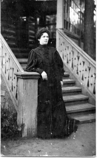 Женщина в рост в темном платье стоит на ступеньках дома, 1910 - 1917