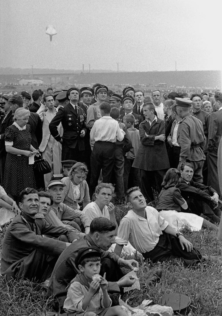 Многочисленные зрители внимательно следят за массовым десантом парашютистов в День авиации на Центральном аэродроме в Тушине, август 1946, г. Москва. Выставка «Парашютисты» с этой фотографией.
