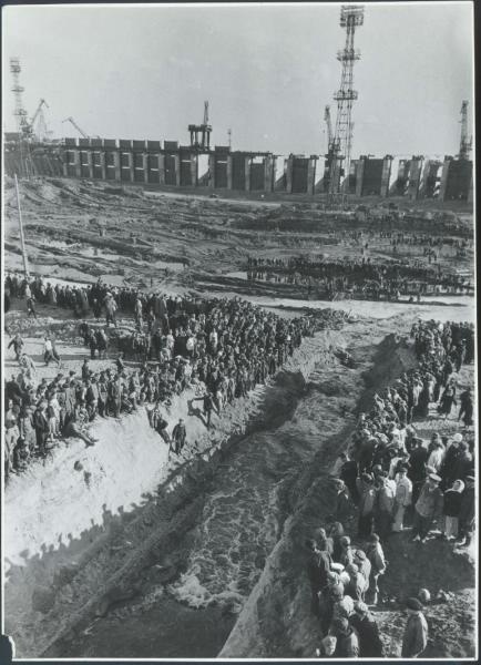 Каховский гидроузел. Затопление котлована, 1955 год, Украинская ССР, Новая Каховка. Строители стоят вдоль русла с протоком, по которому течет вода. Впереди в отдалении – стройка плотины Каховской ГЭС.