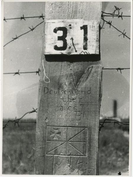 Колючая проволока и столб № 31, 1944 - 1945. Надпись на столбе: «Deutschland über alles (Германия превыше всего)».Выставка «Холокост» с этой фотографией.&nbsp;