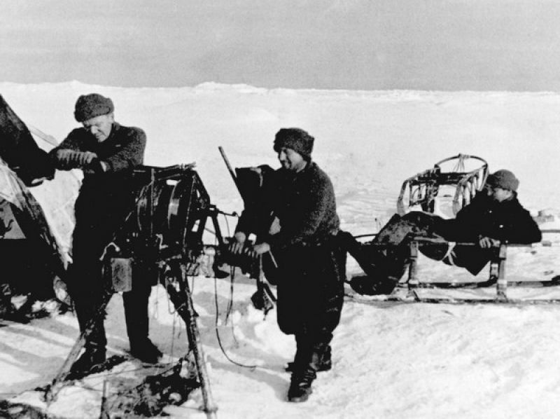 Эрнст Кренкель и Иван Папанин за измерениями глубины океана с помощью ручной лебедки. На нартах отдыхает Евгений Федоров, 1937 год
