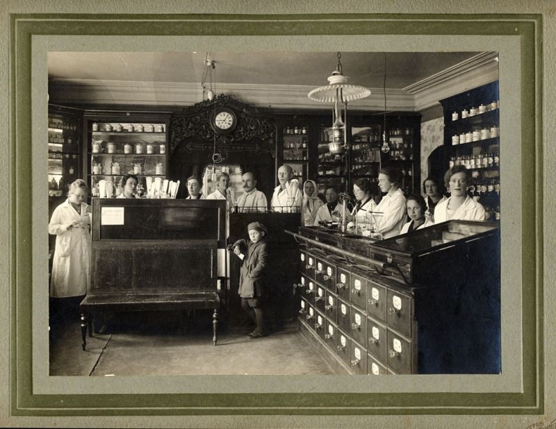 Группа сотрудников в интерьере аптеки. 4-я слева - Мария Александровна Антоненко-Зощенко - бывшая владелица аптеки, 1924 - 1928, Владимирская губ., г. Муром. Выставка «Аптеки ХХ века» с этой фотографией.