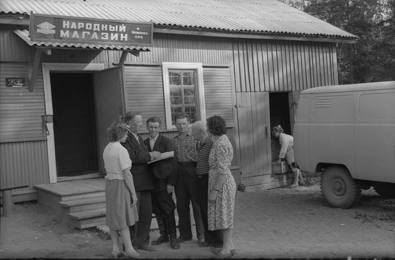 Группа людей около «Народного магазина», 1950-е. Около двери в складское помещение магазина молодая женщина выгружает ящики из УАЗ-450 «Буханка».